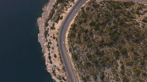 岩の多い海岸沿いの山道を進む車のドローンからの空中風景. — ストック動画