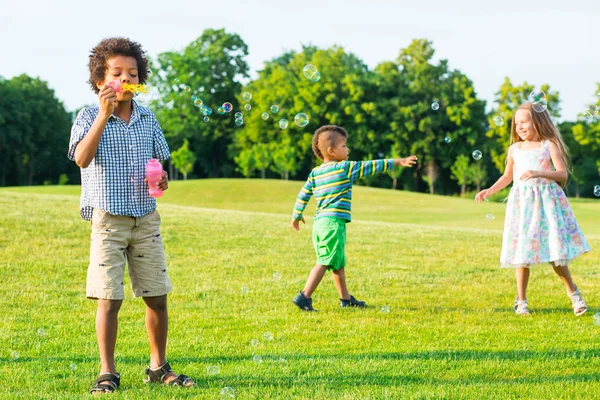 Three kids on the glade with soap bubble. — Stockfoto