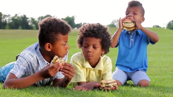 Three mulatto  boys are tasting hamburgers. — Αρχείο Βίντεο