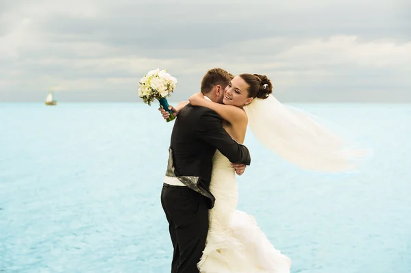 Nice newlyweds are holding each other on the sea background. — Stock Photo, Image