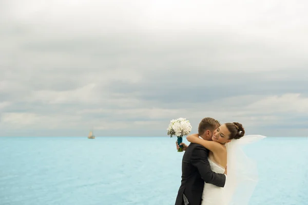 The groom is holding her bride on the sea background. — Stock Photo, Image