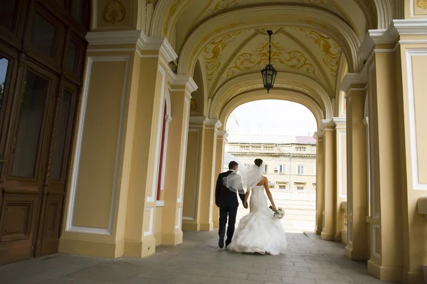 Nice newlyweds are walking under church  arches. — Stock Photo, Image