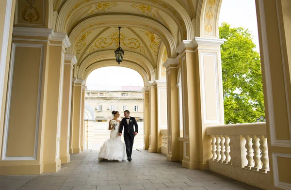 Lindos recién casados están caminando bajo los arcos de la iglesia . —  Fotos de Stock