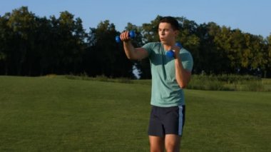 Adam bir çimenlikte dumbbells ile.