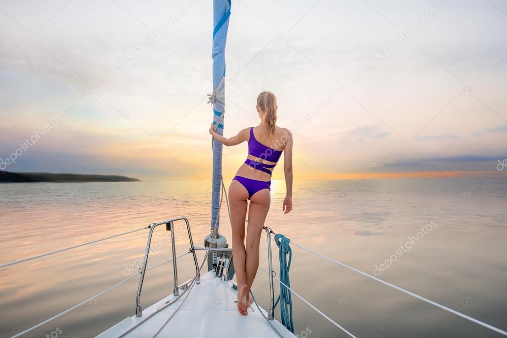 Girl stands on the nose of the yacht and looking at the sunset.