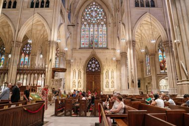 New York City, New York, ABD - 07.31.2024: Bu fotoğraf New York 'taki St. Patricks Katedrali' nin içini gösteriyor. Ziyaretçiler Gotik sütunlar, karmaşık vitraylar ve kutsal camlarla çevrili süslü sahanlıkta oturuyorlar ve yürüyorlar.