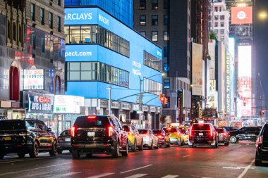New York City, New York, ABD - 07.31.2024: Times Meydanı 'nda kırmızı ışıkta parlayan reklam panoları ile çevrili bir sıra araba ve taksi bekliyor. İkonik mavi Barclays binası ve NYC Mega Mart mağazası önü aydınlık.