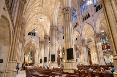 New York City, New York, ABD - 07.31.2024: Fotoğraf, yükselen sütunlar ve renkli camlarla muhteşem bir katedralin içini çeker. Ziyaretçiler mimariye hayran kalıyor ve huzurlu bir atmosferde ahşap sıralarda oturuyorlar..