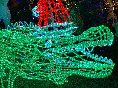 Parlayan ışıklardan yapılmış parlak yeşil bir timsah, neşeli bir Noel sahnesini süslüyor. Aydınlatılmış sürüngen, bayram kutlamalarına tropik bir renk katıyor..
