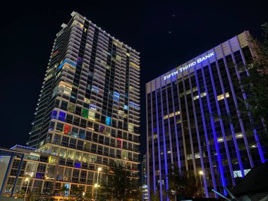 Orlando, Florida, ABD - 11.28.2024: Uzun modern binalar koyu gökyüzüne karşı mavi ve renkli ışıklarla parıldıyor. Gece şehir sahnesi mimariyi ve şehir yaşam tarzını ön plana çıkarıyor.
