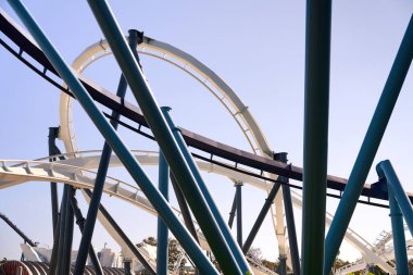 Birbirine bağlı döngüler ve destekler soyut bir çelik ağ oluşturur. Modern lunapark treni tasarımı açık mavi gökyüzüne karşı duruyor..