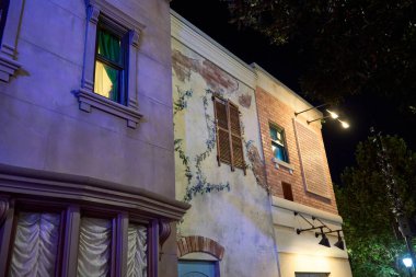 Sarmaşık ve kırsal panjurlu yıpranmış duvarlar süslü pencerelerin yanında duruyor. Karışık malzemeler ve gece ışıkları tarihi şehir karakterini gösteriyor.