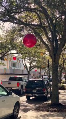 Winter Park, Florida - 11.23.2023: Kırmızı ve altın süslerle süslenmiş meşe ağaçlarının altından geçen park halindeki arabalarla dolu tuğla bir sokak. Mağazalar, trafik ışıkları ve yumuşak gölgeler canlı bir şehir manzarası yaratır..