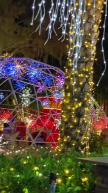 Orlando, Florida - 12.09.2023: Bir jeodezik kubbe gece yıldız patlaması ışık küreleri ve çok renkli LEDlerle doludur. Palmiye gövdeleri ışıklara sarılmış ve iplikçikler parlak bir festival sahnesi oluşturuyor..