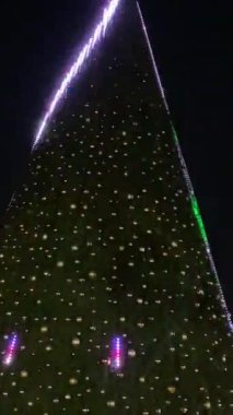 Büyük bir Noel ağacı parlayan ışıklar ve parlak süslemelerle kaplıdır. Karanlık gece arkaplanı dekorasyonları şenlikli renklerle parıldatıyor..