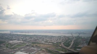 Gün batımında bulutlu bir gökyüzünün altında geniş bir nehri geçen köprüleri olan bir şehrin manzarası. Otoyollar ve yerleşim alanları aşağılara yayıldı.