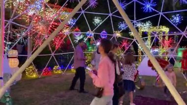 Orlando, Florida, ABD - 12.12.2023: İnsanlar renkli tatil ışıkları ve parıltılı yıldız patlaması dekorasyonlarıyla çevrili jeodezik bir kubbenin içinde toplanıyorlar. Açık hava Noel eğlencesi geceleri şenlikli tesisler ve kış neşesiyle parlıyor..