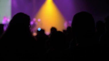 Konsere gidenlerin koyu renk siluetleri sahnede parlak sarı bir spot ışığıyla bir performans izliyorlar. Mor ışıklandırma, sis ve bokeh dramatik bir canlı müzik havası yaratır..