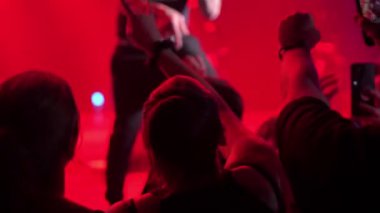 Heyecanlı hayranlar canlı bir gösteri sırasında ellerini kaldırıyorlar. Sahne güçlü bir kırmızı konser ışığı ve sisle aydınlandı..