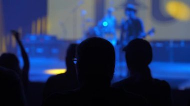 Konsere gidenlerin karanlık siluetleri ön planı doldururken bir grup sahnede bulanıklaştı. Mavi ışık ve sis mekan içinde dramatik bir canlı müzik ortamı yaratır..