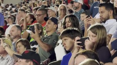 Orlando, Florida, ABD - 03.02.2024: Seyirciler canlı bir stadyum etkinliği sırasında fotoğraf ve video çekmek için akıllı telefonları soyuyor. Seyirci koltuklarından anı çekerken aktif olarak meşgul oluyor..