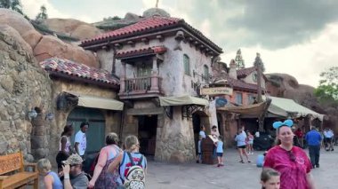 Orlando, Florida, ABD - 05.06.2024: Adventure Park 'ta terasotta çatısı ve balkonu olan taş duvarlı bir köy binası. Konuklar bulutlu bir Orlando öğleden sonra, haritanın yanındaki meydanda dolaşırlar..