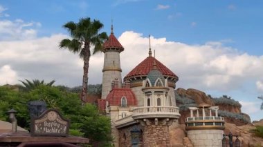 Orlando, Florida, ABD - 05.06.2024: Disney Magic Kingdom 'daki palmiye ağaçlarının üzerinde peri masalı kuleleri ve taş kuleler yükseliyor. Temalı kale mimarisi Orlando, Florida 'da mavi gökyüzüne karşı duruyor..