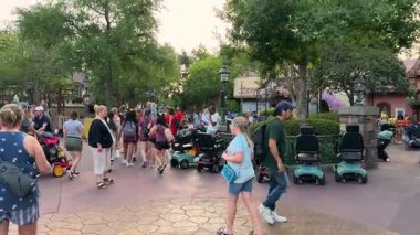 Orlando, Florida, ABD - 05.06.2024: Ziyaretçiler, aileler ve çocuklar Macera Parkı 'ndaki gölgeli bir Fantasyland geçidini doldurdular. Gezginler, mobiletler ve köy teması hareketli bir tatil sahnesi oluşturur..