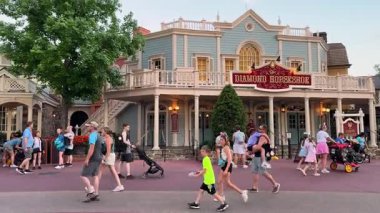 Orlando, Florida, ABD - 05.06.2024: Konuklar Özgürlük Meydanı 'ndaki Diamond Horseshoes Viktorya dönemi cephe ve balkonunun önünden geçtiler. Canlı sokak sahnesinde aileler, tabela ve sıcak akşam ışıkları yer alıyor..