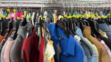 Orlando, Florida, ABD - 07.09.2024: Çeşitli gömlekler, kazaklar ve ceketler ikinci el giyim mağazasında metal bir askıda sıkıca asılı duruyor. Farklı renkler, kumaşlar ve stiller ikinci el moda çeşitliliğini gösteriyor.