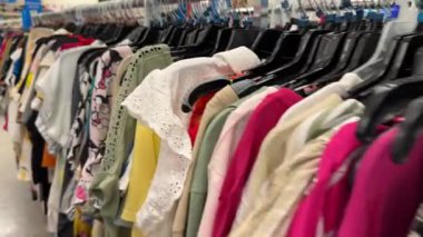 Uzun bir ikinci el kadın bluzu ve süveter rafı ikinci el veya ikinci el ürünler satan bir mağazada sıkıca asılı duruyor. Farklı kumaşlar, renkler ve desenler giyim reyonunu dolduruyor..