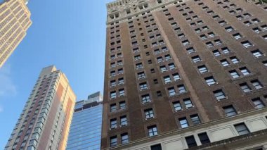 Empire State Binası modern cam ve tuğla gökdelenlerle birlikte New York şehir merkezinin üzerinde yükselir. Sıcak gün batımı ışığı, açık mavi gökyüzüne karşı yüksek kuleleri vurgular..