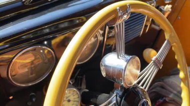Orlando, Florida, ABD - 02.03.2024: Eski bir arabanın iç kısmı krom telli sarı bir direksiyon ve monte edilmiş bir saat gösteriyor. Retro göstergeler, parlak siyah gösterge paneli ve ılık süslemeler bu klasik otomobilin zarif tasarımını vurguluyor.