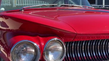 Parlak kırmızı klasik araba ön tarafında iki yuvarlak far, krom süsleme ve oyulmuş bir kaput var. Parlak boya ve kıvrımlı ızgara hatları klasik otomobil tasarımını vurguluyor.