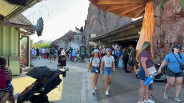 Orlando, Florida, ABD - 08.31.2024: Turistler Disney Springs 'teki kayalık bir şelalenin önünden geçen yoğun bir patika boyunca yürüyorlar. Dükkanlar, bebek arabaları ve aileler açık hava eğlence parkı sahnesini dolduruyor..
