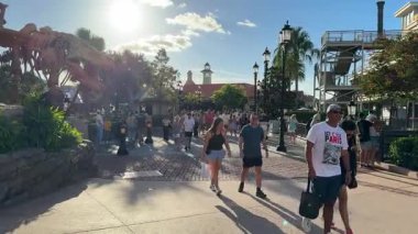 Orlando, Florida, ABD - 08.31.2024: Yoğun temalı bir park yolu üzerinde büyük bir dinozor iskeleti beliriyor. Turistler, palmiyeler, ışıklar ve dükkanlarla çevrili güneşli öğleden sonra güneşinin altında yürürler..