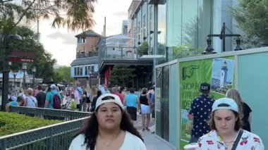 Orlando, Florida, ABD - 08.31.2024: Kalabalık kalabalık bir kalabalık şehir eğlence bölgesinde kalabalık bir alışveriş caddesi boyunca yürüyor. Cam binalar, tabelalar ve yeşillik, canlı bir tatil yeri ortamı yaratır..