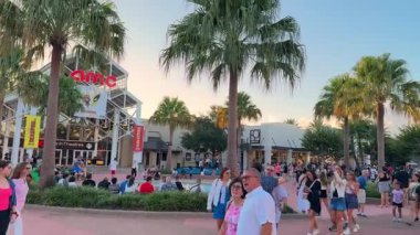 Orlando, Florida, ABD - 08.31.2024: Orlando, Florida 'daki Disney Springs' de AMC tiyatrosu ve palmiye ağaçları yakınında büyük bir kalabalık toplandı. İnsanlar sıcak bir akşamda meydanda gezinir, konuşur ve dinlenir..
