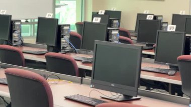 Orlando, Florida, ABD - 03.13.2024: Masaüstü bilgisayarları, numaralandırılmış çalışma istasyonları olan boş bir bilgisayar laboratuvarında hazır bekliyor. Sessiz sınıf ayarları teknoloji, eğitim ve test hazırlıklarını vurguluyor.