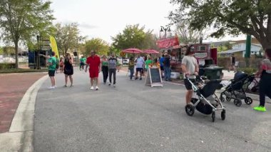 Orlando, Florida, ABD - 03.16.2024: İnsanlar kalabalık bir sokak festivalinde yemek kamyonları ve büfelerin önünden geçiyor. Çocuklu ve bebek arabalı aileler gün ışığında atıştırmalık ve içeceklerin tadını çıkarıyorlar..