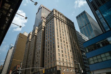 Aşağıdan bakıldığında Manhattan şehir merkezindeki tarihi tuğla binalar ve modern cam kuleler görülüyor. Parlak gökyüzü ve keskin açılar şehrin çeşitli mimarisini vurgular.