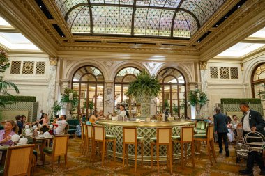 New York City, New York, ABD - 08.01.2024: Lüks bir otel salonu, şık dekorlar ve yemek ve içeceklerden keyif alan konuklarla çevrili, merkezde yuvarlak bir bara sahiptir. Süslü iç mekânda kemerli pencereler, çiçek aranjmanları ve lekeli...