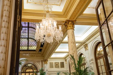 Tarihi lüks bir otelin tavanına asılmış zarif kristal bir avize. Mermer sütunlar, boyalı camlar ve klasik mimari müsrif bir iç atmosfer yaratır..