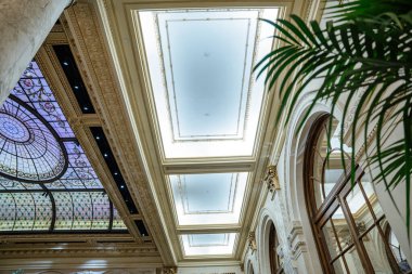 Mozaik cam paneller, süslü pervazlar ve kemerli pencerelerin bulunduğu tarihi bir otel tavanının zarif manzarası. Mimari tasarım, lüks elementleri klasik sanatçılık ve doğal ışık ile birleştirir..