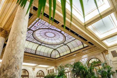 Detaylı desenli muhteşem vitraylı kubbe tarihi lüks bir otel lobisini taçlandırıyor. Mermer kolonlar, kemerler ve kapalı bitkiler rafine mimari bileşimi tamamlar.