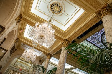 Zarif kristal avizeler, altın süslemeli ve klasik kalıplı zengin ve detaylı bir tavandan sarkıyor. Lüks otel iç mekanında mermer sütunlar, kemerli kapılar ve boyalı cam paneller bulunur..