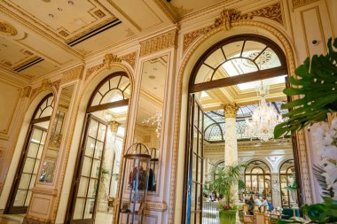 New York City, New York, ABD - 08.01.2024: Yüksek kemerli kapılı büyük bir giriş, avizeler, mermer sütunlar ve boyalı camlarla süslenmiş lüks bir otel salonuna açılıyor. Süslü aynalar ve klasik detaylar üst sınıf ambiyansı yansıtır.