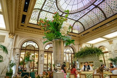 New York City, New York, ABD - 08.01.2024: Gümüş bir vazodaki büyük bir çiçek düzenlemesi vitray tavanlar ve klasik mimariyle lüks bir restoranı dekore eder. Lokantalar yemeklerini yeşillik ve süslemelerle dolu zarif bir ortamda yerler.