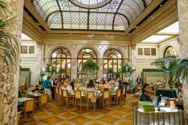 New York City, New York, ABD - 08.01.2024: Büyük bir restoran yemek ve içeceklerden keyif alan insanlarla çevrili merkezi bir bara sahiptir. Mekan mermer sütunlar, çiçek düzenlemeleri ve boyalı cam kubbeyle zengince dekore edilmiş..