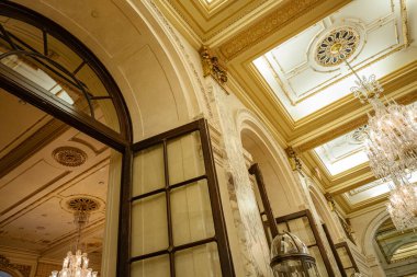 Zarif bir salon, kemerli ahşap kapılar, karmaşık altın tavan detayları ve parıldayan kristal avizeler. Klasik mimari elementler ve mermer sütunlar lüks ve zamansız bir ortam yaratır..